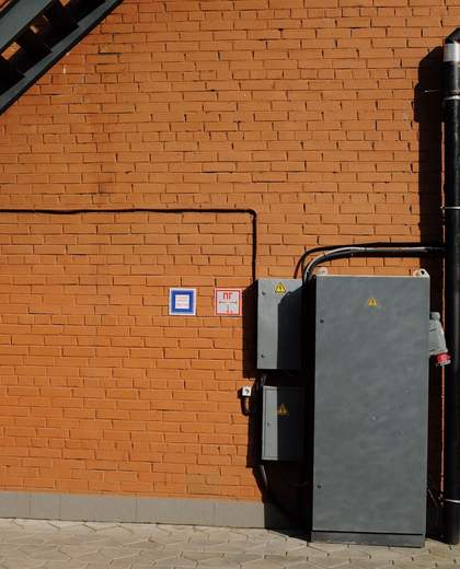 Coffret électrique et gaines fixés sur une façade en brique