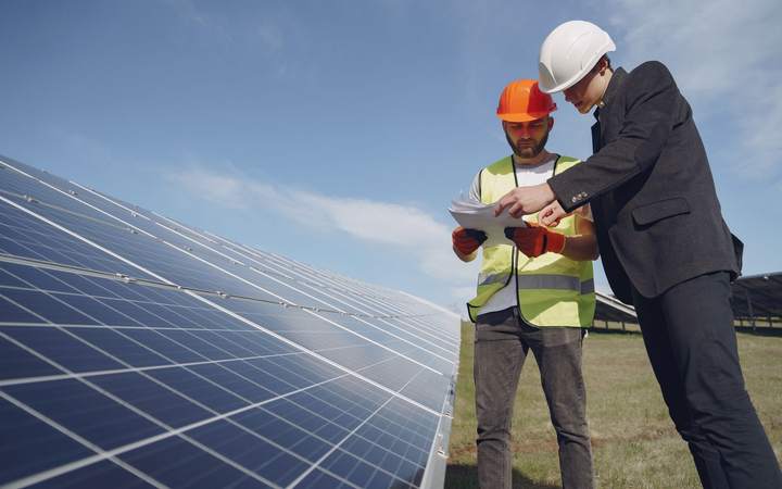 Technicien casqué en gilet haute visibilité et ingénieur consultant un plan devant des panneaux solaires