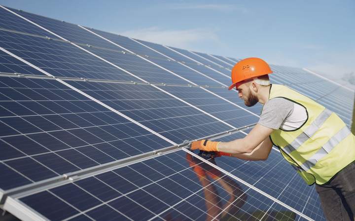 Technicien casqué et en gilet haute visibilité contrôlant un panneau d’une centrale photovoltaïque