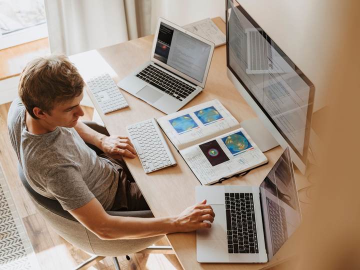 Homme travaillant sur plusieurs ordinateurs portables à un bureau vu d’en haut