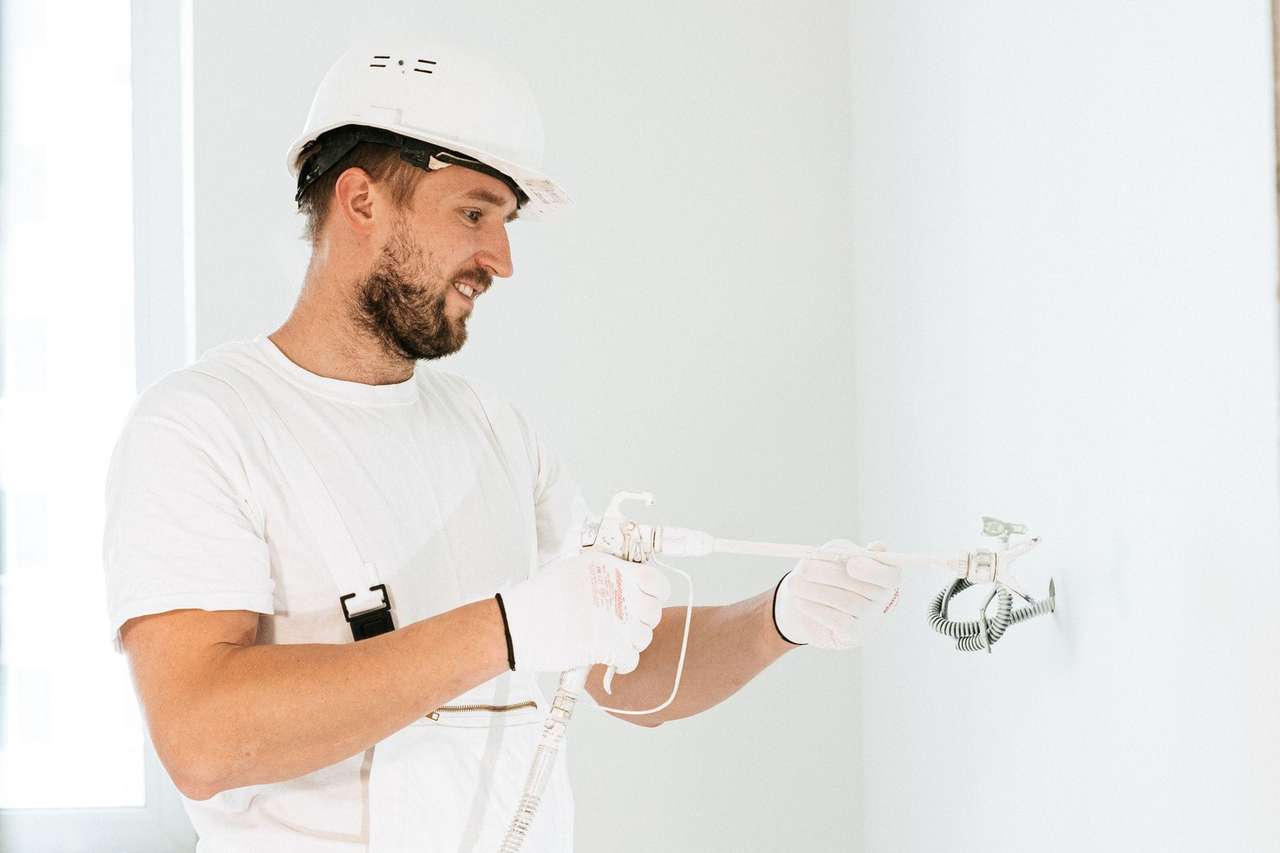 Électricien casqué et ganté raccordant un point lumineux au mur