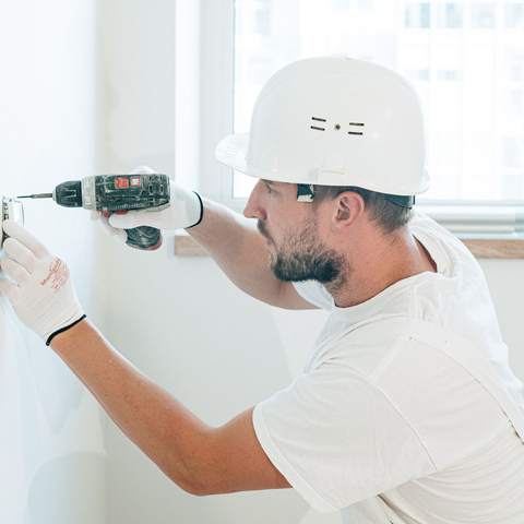 Électricien casqué fixant un boîtier électrique au mur d’un logement en travaux