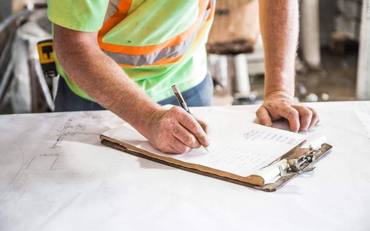 Mains d’un ouvrier en gilet haute visibilité remplissant un document sur plans de chantier