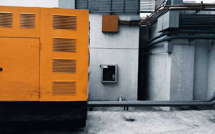 Groupe électrogène industriel orange installé contre un local technique relié par des conduites