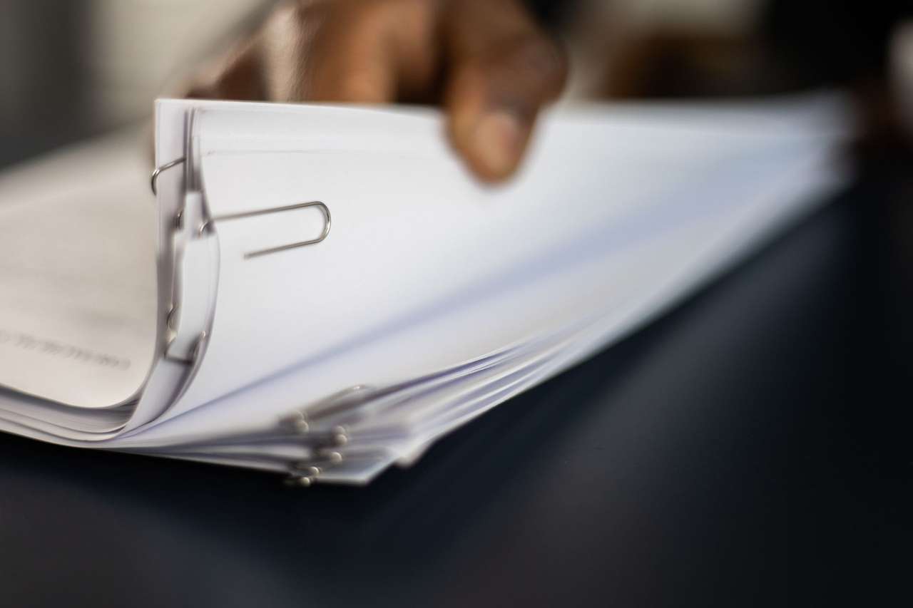 Main feuilletant une liasse de documents retenus par une pince sur un bureau