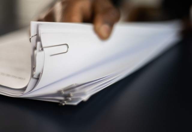 Main feuilletant une liasse de documents retenus par une pince sur un bureau