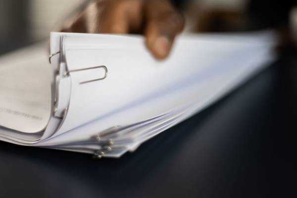 Main feuilletant une liasse de documents retenus par une pince sur un bureau