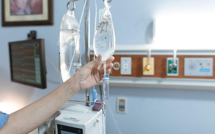 Main d’une soignante réglant une poche de perfusion près d’une rampe de fluides médicaux