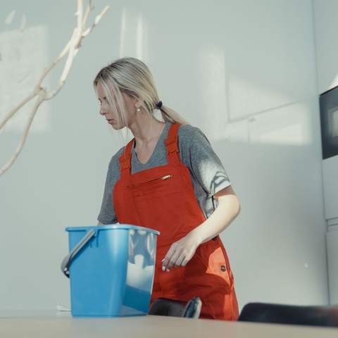 Agente d’entretien en tablier de travail avec un seau, dans un local lumineux