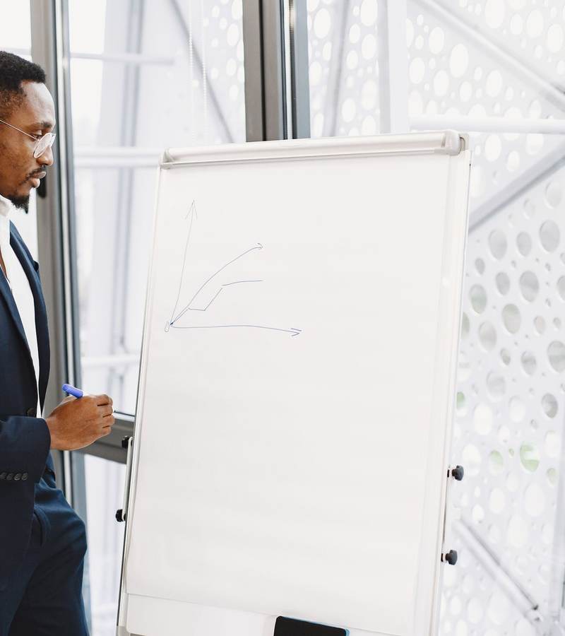 Formateur en costume de profil écrivant sur un paperboard dans une salle lumineuse
