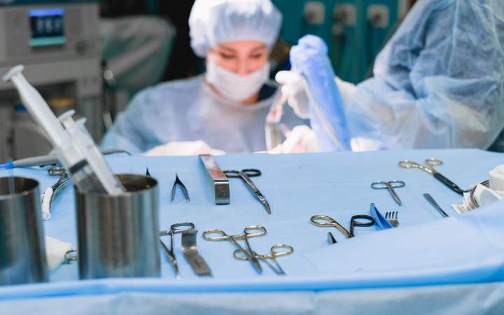 Instruments chirurgicaux alignés sur un champ stérile bleu devant une infirmière de bloc masquée