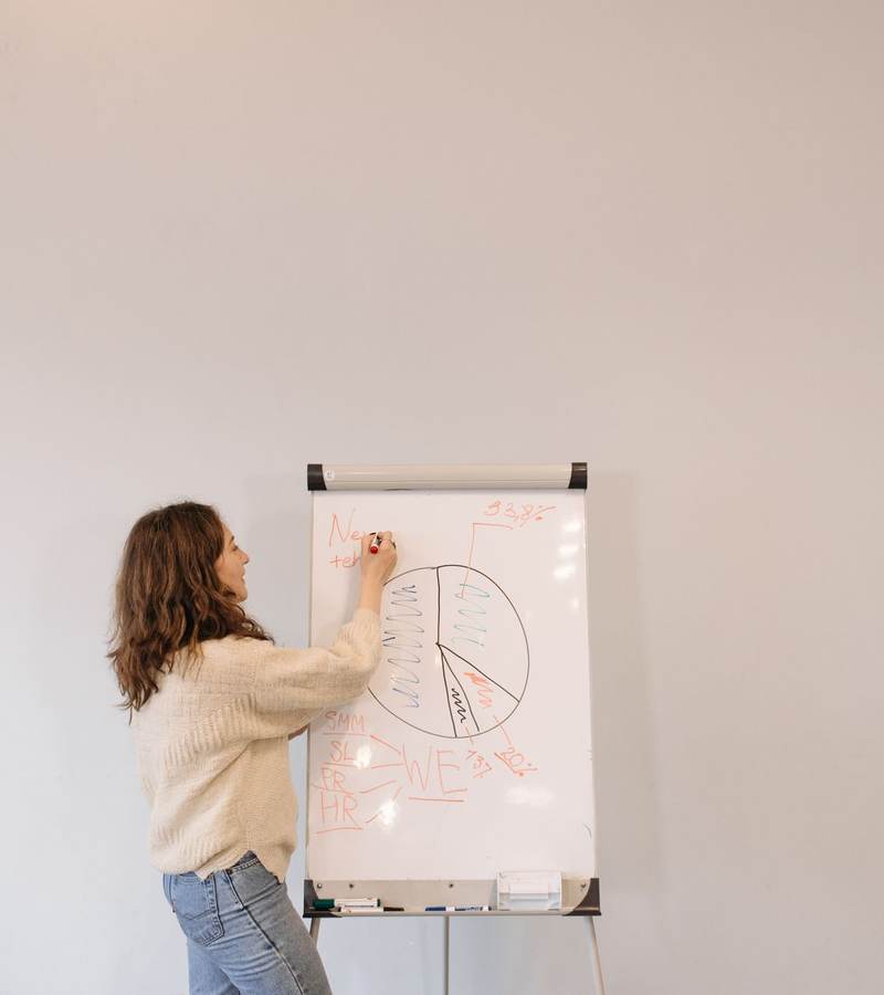 Personne de dos dessinant un schéma sur un paperboard dans une salle claire