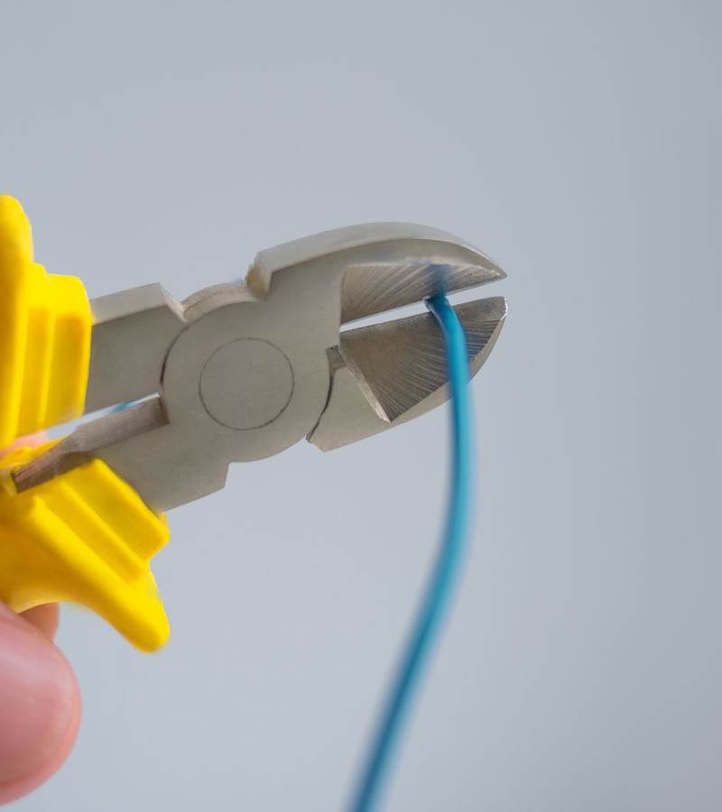 Main tenant une pince coupante jaune pour sectionner un fil électrique bleu