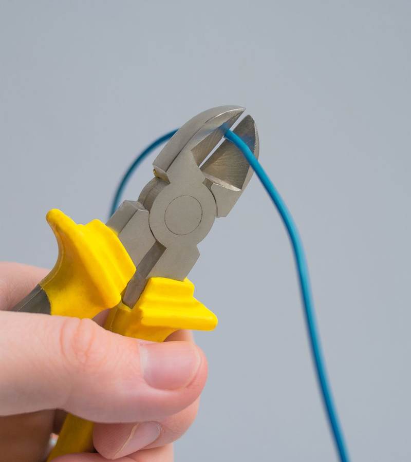 Main utilisant une pince coupante à poignées isolées pour sectionner un fil électrique