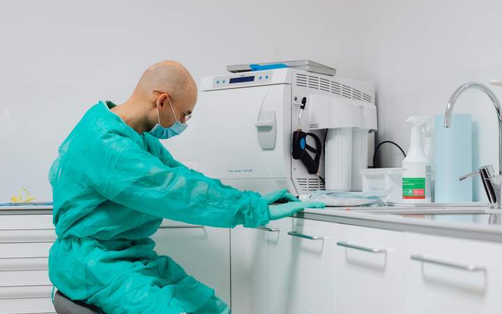 Technicien en tenue verte et masque travaillant près d’un appareil de stérilisation au laboratoire
