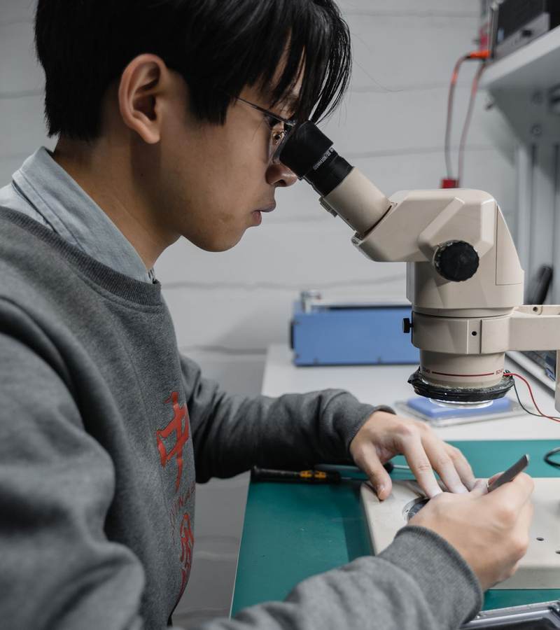 Technicien de laboratoire examinant un composant électronique au microscope sur un plan de travail antistatique