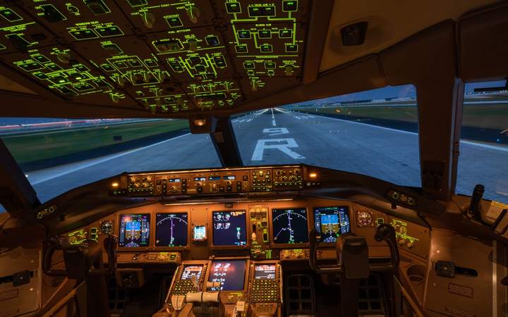 Poste de pilotage d’un avion de ligne éclairé, face à la piste au crépuscule