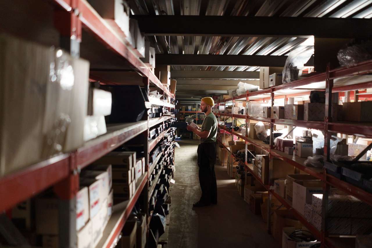 Magasinier consultant un document entre des rayonnages chargés de cartons