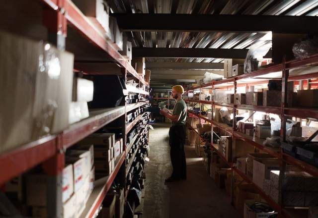 Magasinier consultant un document entre des rayonnages chargés de cartons