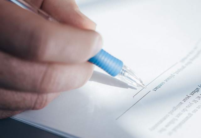 Gros plan sur une main signant un document au stylo bille bleu