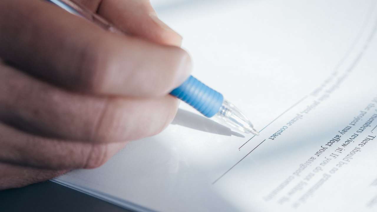 Gros plan sur une main signant un document au stylo bille bleu