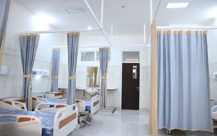 Salle d’hospitalisation avec lits médicalisés séparés par des rideaux bleus