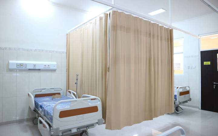 Chambre d’hôpital avec lits séparés par un rideau beige