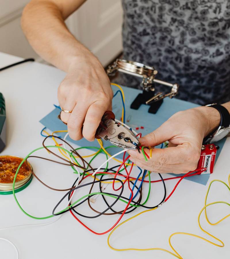 Mains manipulant des fils électriques colorés et un petit boîtier sur un plan de travail