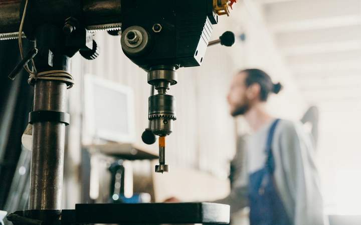 Perceuse à colonne en premier plan avec un opérateur en bleu de travail dans l’atelier