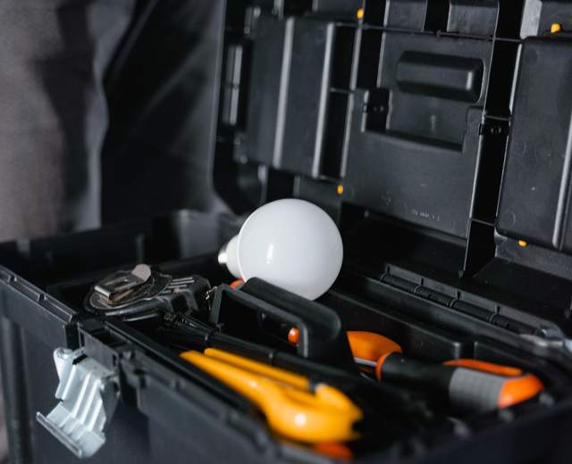 Caisse à outils ouverte contenant une ampoule, des pinces et des tournevis à manche orange