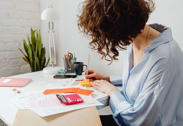 Femme de dos travaillant sur des papiers et une calculatrice à son bureau lumineux