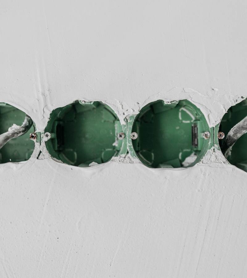 Boîtes d’encastrement vertes alignées dans un mur blanc avec gaines électriques en attente
