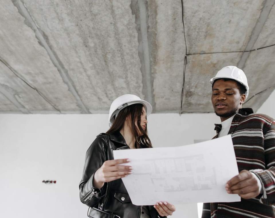 Deux personnes casquées étudient un plan dans un bâtiment en travaux