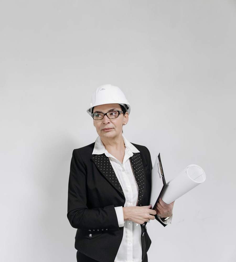 Responsable de travaux en casque blanc tenant des plans devant un mur blanc