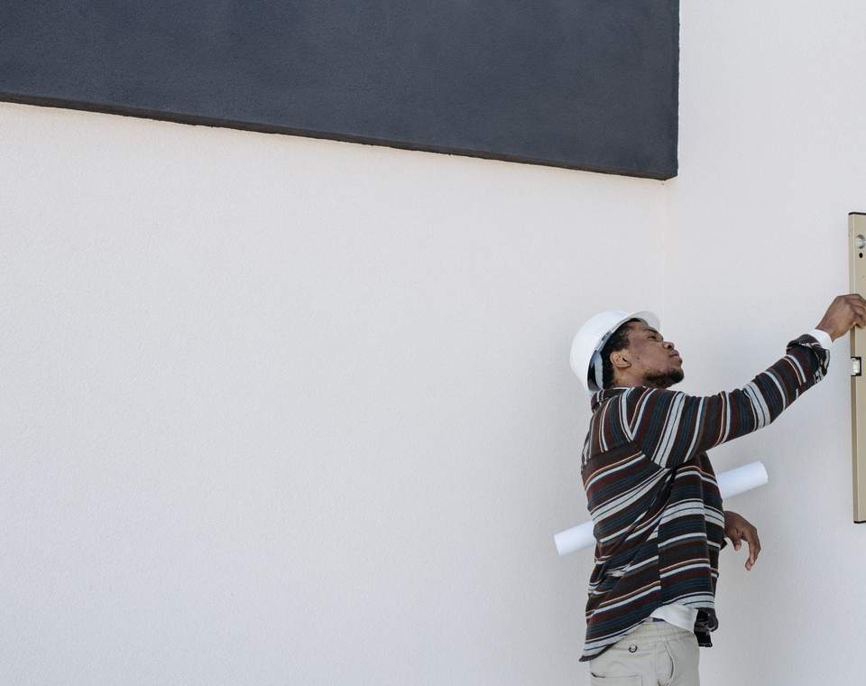 Ouvrier casqué contrôlant l’aplomb d’un mur blanc avec un niveau