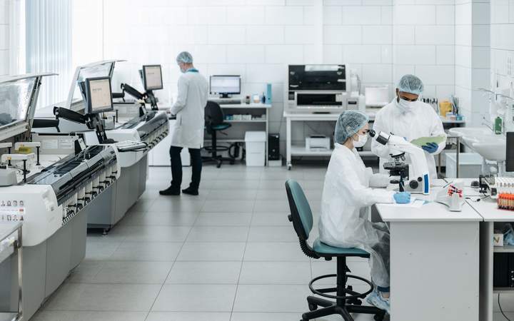 Techniciens en blouse et charlotte dans un laboratoire équipé d’analyseurs et de microscopes