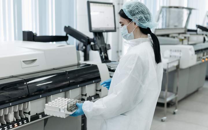 Technicienne de laboratoire en charlotte et masque chargeant des tubes dans un analyseur automatisé