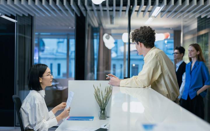 Accueil d’un immeuble de bureaux vitré où des visiteurs échangent avec une hôtesse