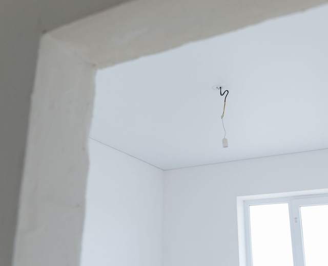 Douille provisoire suspendue au plafond d’une pièce en travaux, fenêtre lumineuse