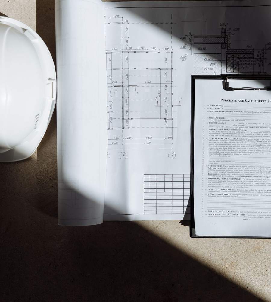 Casque de chantier blanc posé sur des plans et un dossier de formation, en lumière rasante