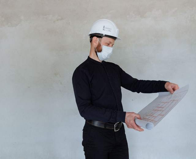 Professionnel casqué consultant un plan de câblage devant un mur gris clair