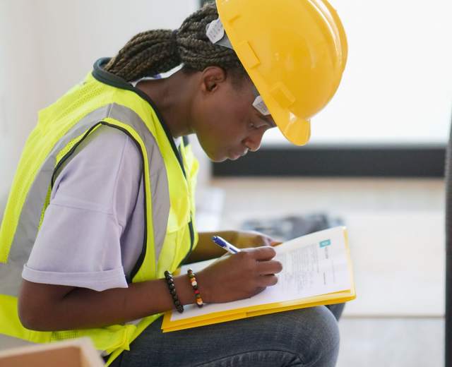 Technicienne en casque et gilet haute visibilité remplissant un formulaire