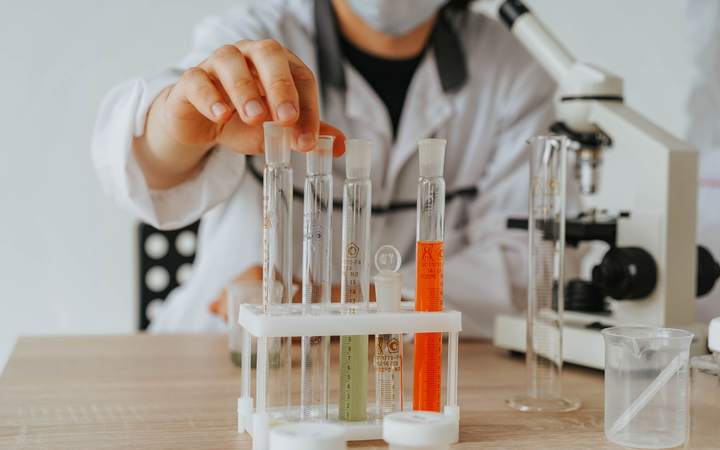 Chercheur en blouse plaçant des éprouvettes graduées sur un portoir à côté d’un microscope