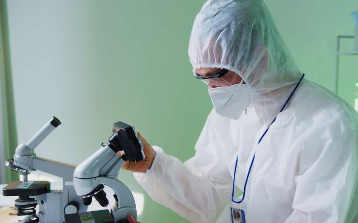 Chercheur en combinaison de protection et masque observant au microscope dans un laboratoire