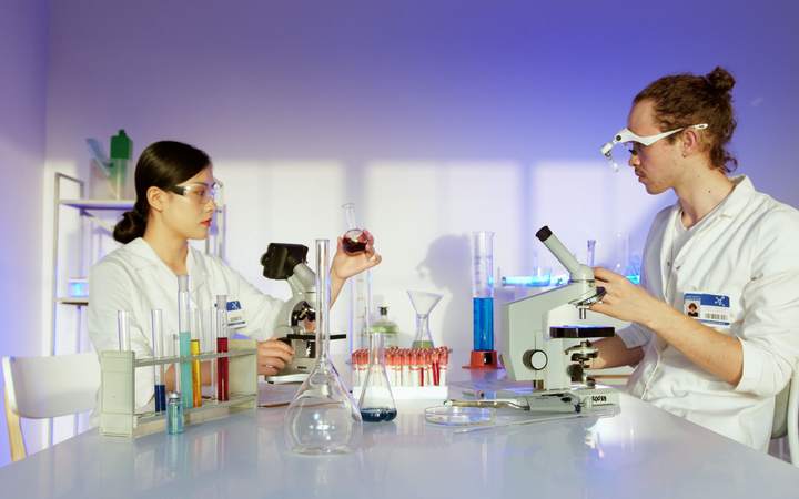 Deux chercheuses en blouse et lunettes de protection manipulent échantillons et microscope au laboratoire