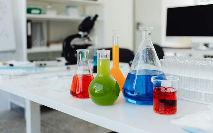 Verrerie de laboratoire remplie de liquides colorés posée sur une paillasse blanche de recherche