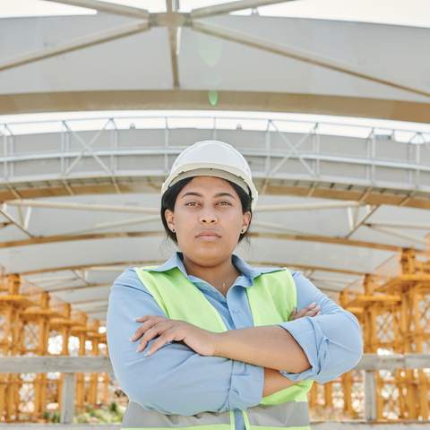 Cheffe de chantier casquée en gilet haute visibilité, bras croisés, sous une charpente