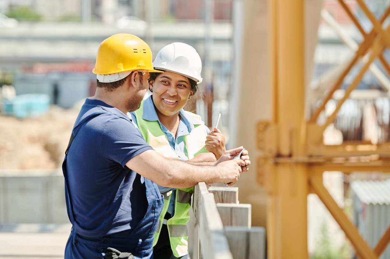 Deux techniciens casqués échangeant en souriant sur un chantier de construction