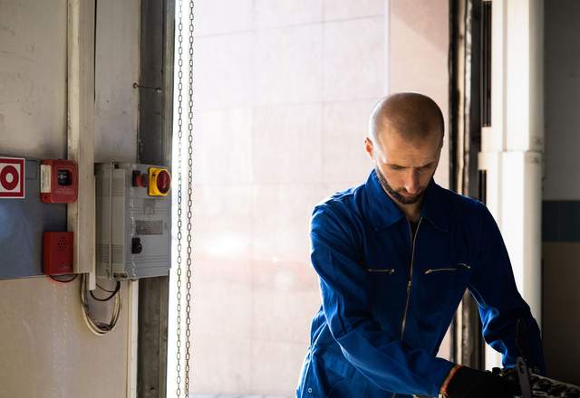 Technicien en combinaison bleue travaillant près de boîtiers de commande fixés au mur d’un local