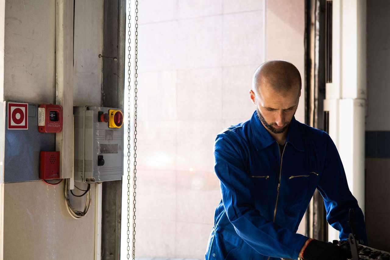 Technicien en combinaison bleue travaillant près de boîtiers de commande fixés au mur d’un local